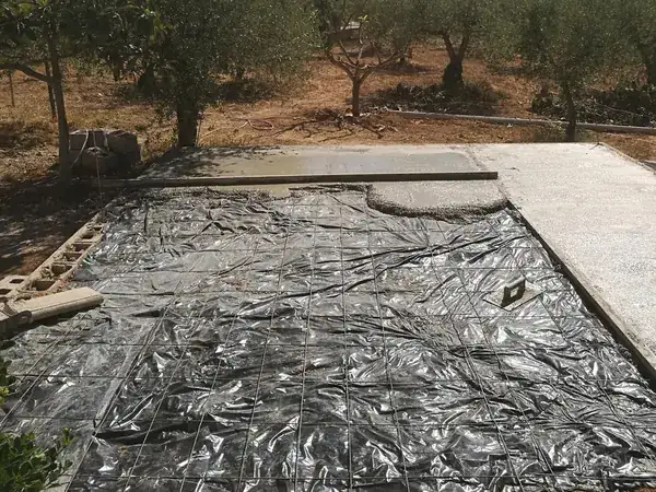 La piscina en obra, cubierta con plástico, en un terreno con olivos